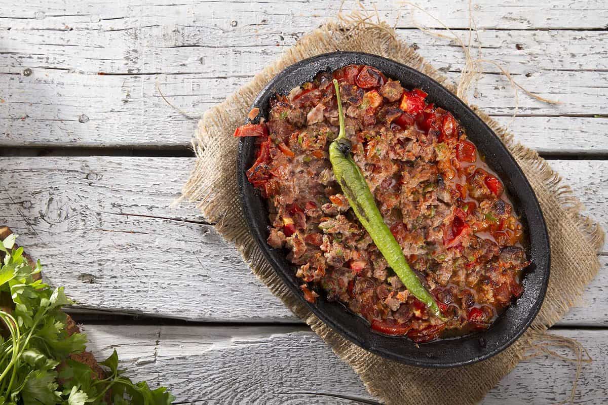 Turkish and Arabic Traditional Ramadan Food Lamb Kavurma Guvec with hot red pepper. Top view on white rustic wood background.
