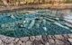 A pool of clear blue water with ancient ruins on the floor, where people are bathing