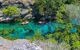 Clear aquamarine water where people are rafting, with trees lining the banks