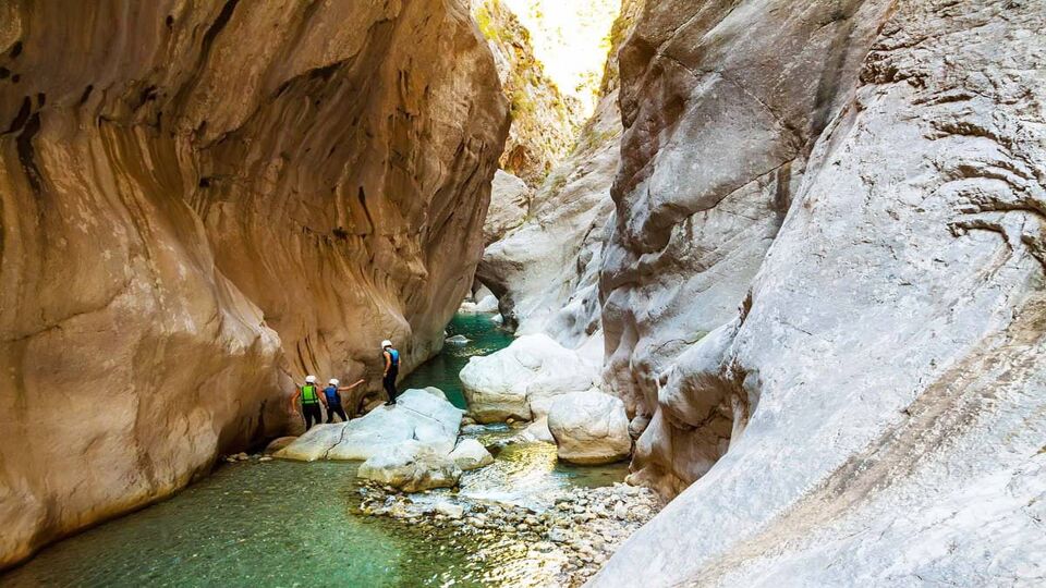 A few tourists wading through water at the bottom of a canyon