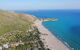 Aerial view of the beach, backed by a green slope with bright blue sea water in front