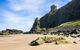 Beach with rocks covered in moss and a building above a tunnel in the daytime