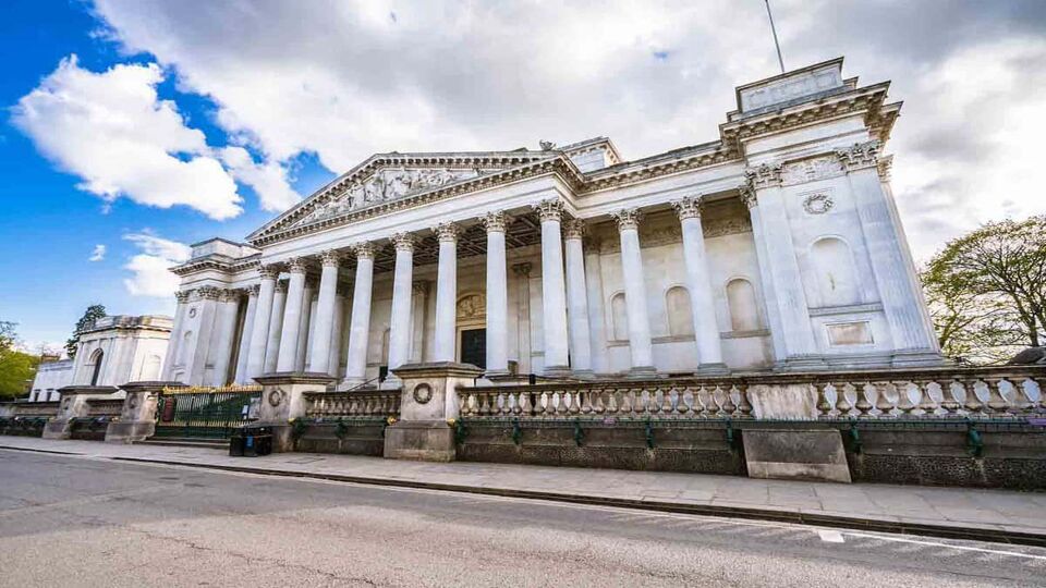 Exterior view of large, white neo-classical museum whose entrance is fronted by pillars