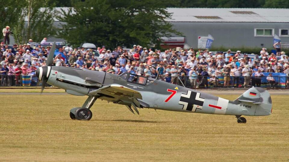 small plane landing on an open grass space in front of crowds