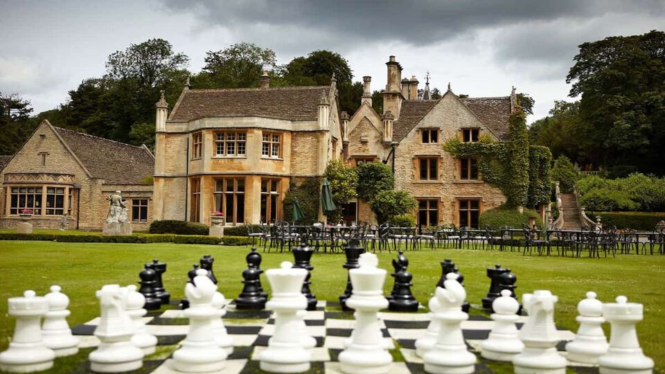 A life size chess board in a garden with a manor in the background.
