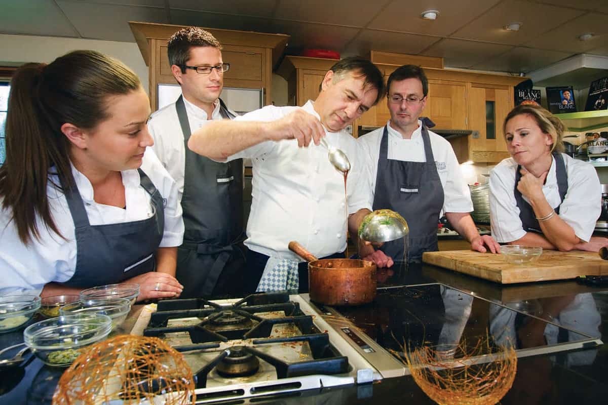 Group of people crowded around an over in the cooking school kitchen