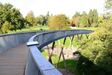 A curved, modern bridge over a lake with many trees in the background.