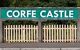 A white Corfe Castle railway station sign on a green background, above a white wooden fence