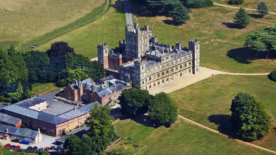 Aerial view of Jacobethan style Highclere Castle surrounded by an open field with some trees scattered around