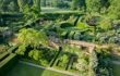 An overview of the Rose Garden from the Tower at Sissinghurst Castle Garden. There are multiple bushes, shrubs and trees divided by small hedges. Further towards the background there is a beautifully structured arrangement of hedges.