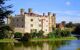 Landscape view of Leeds castle, surrounded by trees and a lake that runs around the castle