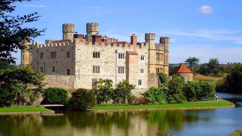 Landscape view of Leeds castle, surrounded by trees and a lake that runs around the castle