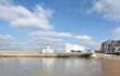A landscape view of Turner Contemporary art gallery in Margate. The foreground shows the sandy beach of margate against the tides, where the gallery can be seen in the distance and reflected on the surface of the waters.