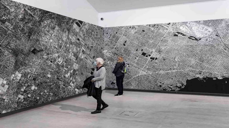 Two women inside Turner Contemporary art gallery looking at the artwork displayed on the walls, at the corner of the room. The artwork is in black and white, filling nearly the entire wall.
