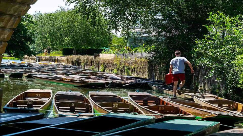 Man walking on punts that are all tied up together underneath the bridge