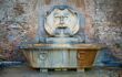 roman fountain with a strange fat face on the wall above an old bath tub