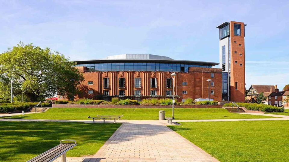 A front view of the Royal Shakespeare Theatre where the pathway stretches towards the building with clean and clear green grass surrounding the pathway and theatre