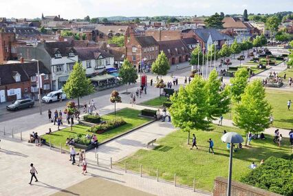 An overview of a public park with a large open grass area with people seated down.