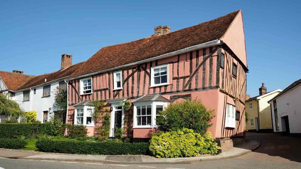 Picturesque image of a pink medieval cottage in Lavenham with a neatly trimmed shrubs at the front of the house.