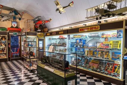 the inside of Brighton Toy and Model Museum. The floor has black and white chequered tiles, and there are model aeroplanes hanging from the ceiling above the till.