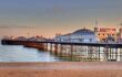 Brighton Pier at sunset. Fairground rides and entrance to the pier visible above the reflective water.