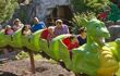 A two seated green dragon rollercoaster filled with a child and their parent beside them