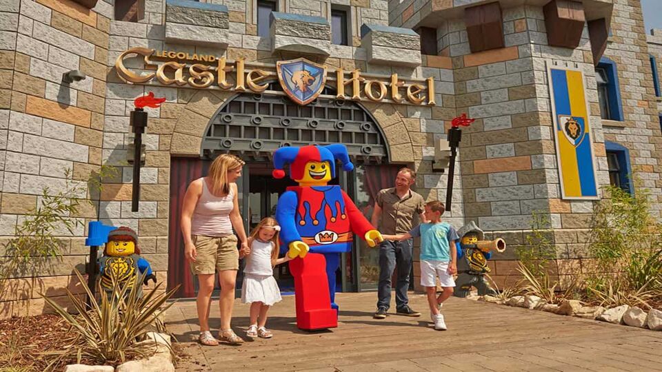 A family stood outside Legoland Castle Hotel with a Lego mascot holding the two children's hand on a sunny day