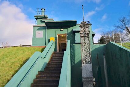 Stairs leading up to a small, teal green entrance to a semi-subterranean bunker
