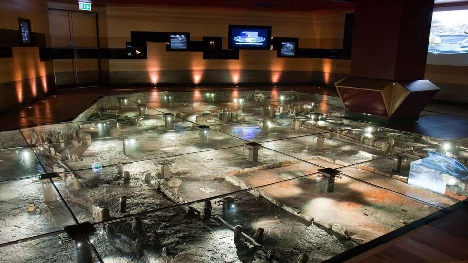 Interior of museum where a glass floor looks through to ruins beneath
