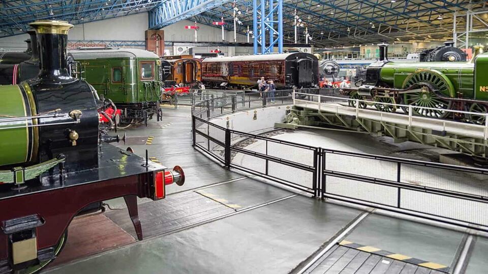 View of various trains inside an exhibition hall, one is rotating on a roundhouse