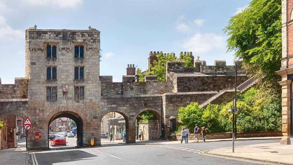 View of Roman walls and ancient gate spanning across a street with a car passing underneath