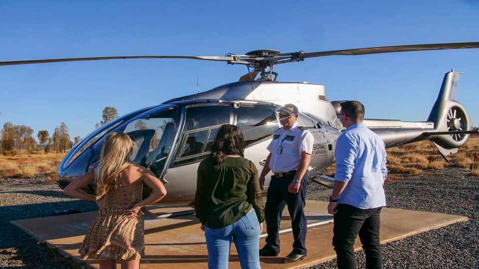A group of people talking to a pilot next to a helicopter.