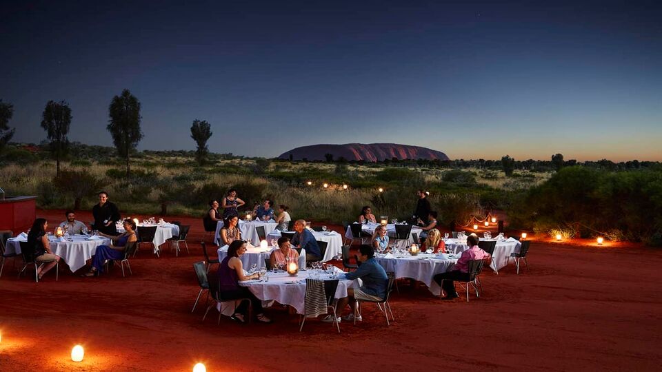People eating at white cloth covered table just after sunset surrounded by cnadlelight, with the backfrop of the desert.