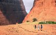 3 people walking to a large red rock formation.