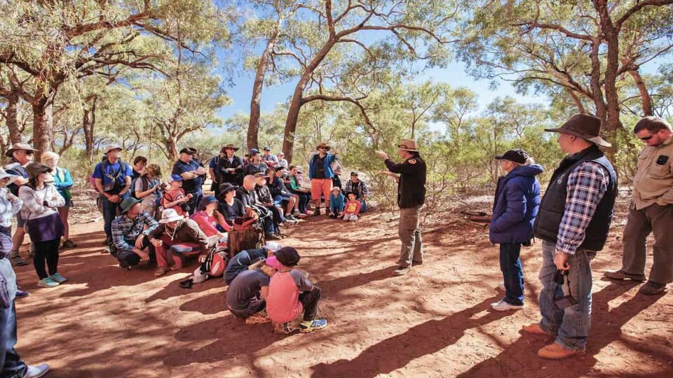 A man giving a talk to a group of people in the desert