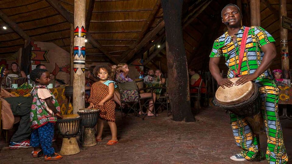 man drumming in traditional dress whilst two children copy