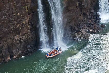 A jetboat with people on the Zambezi river alongside the base of a waterfall