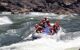 A group on a raft battling the white-water rapids. man at back is steering