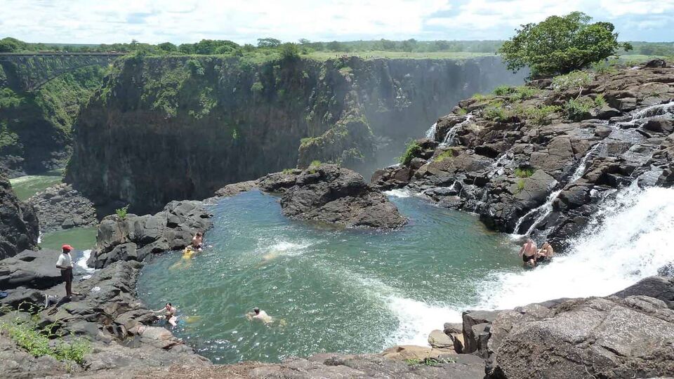 Aerial view down onto a rock pool on top of the waterfall with people swimming in ti