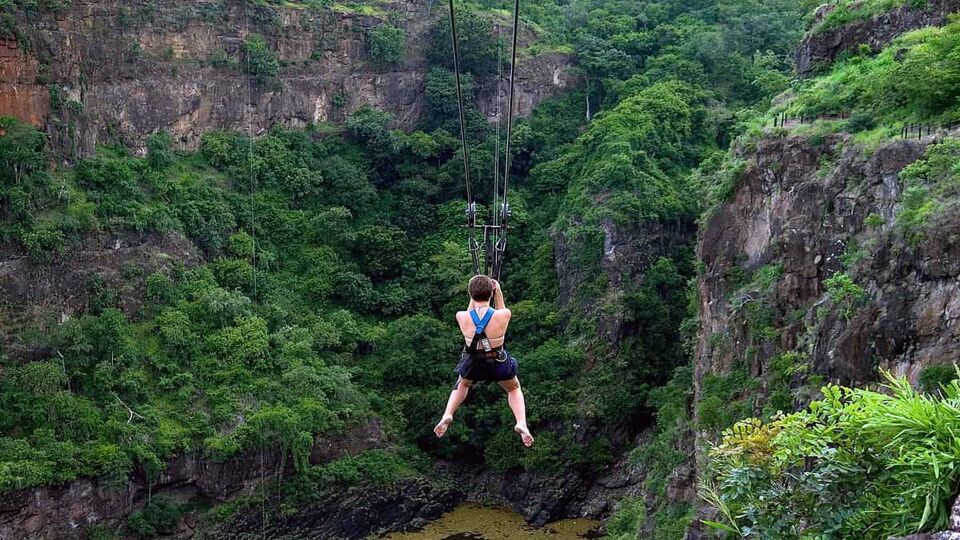 The back of a girl on the zip-line across the Zambezi with forestry below