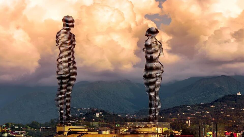 giant man and woman sculpture facing each other with clouds behind