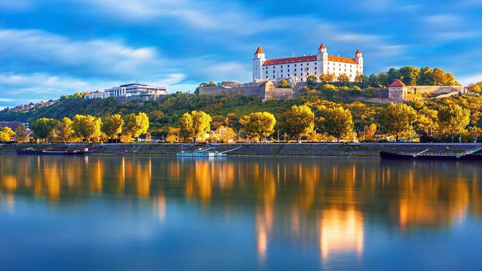 Large white square castle on a forested hill overlooking the river Danube