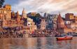 Historic Varanasi city with ancient temples and buildings along the Ganges river ghat as viewed from a boat at sunrise.