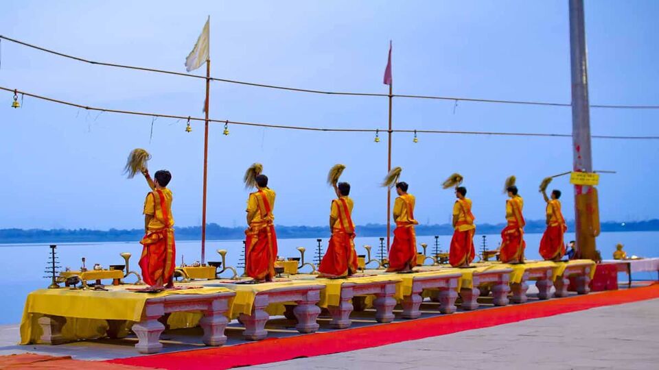 7 men dressed in colourful yellow and red costumes standing looking out at the river , making an offering
