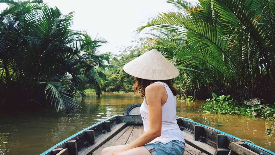 A young woman in a Vietnamese hat rides a boat on the Mekong River in Vietnam