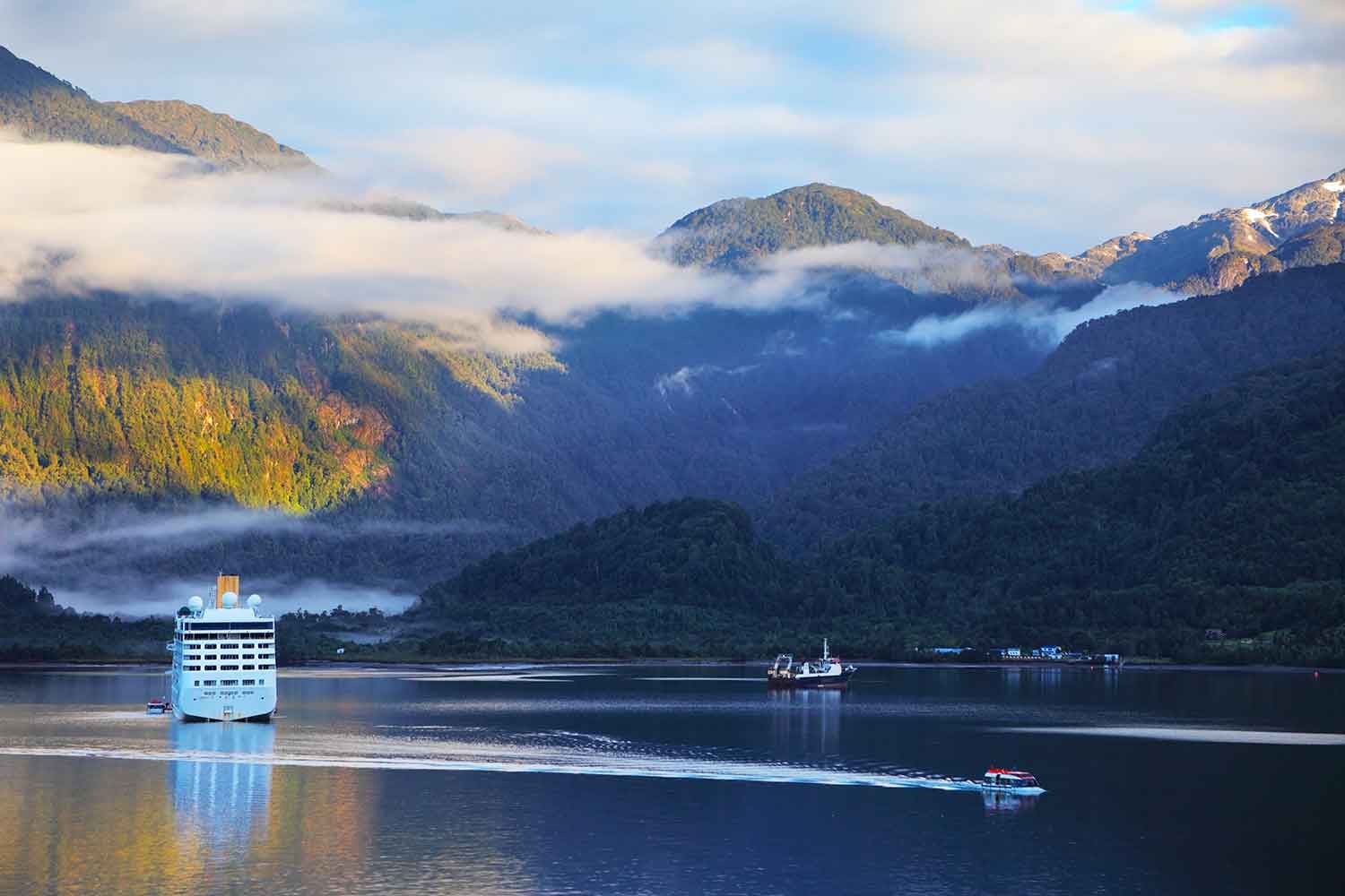 Landscape of giant fjords, glassy water and a cruise ship looking tiny
