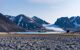 tiny cruise ship sailing before a large glacier and mountains