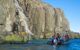 small dingy driving beside the waterfall coming down a cliff into the sea