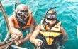 an elderly couple about to snorkel, hanging on side of the boat
