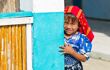a young child in red headress looking around the corner